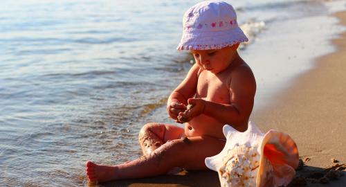 Bambino felice gioca con la sabbia sulla spiaggia, accanto al mare.