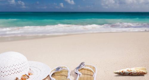 Spiaggia serena con cappello, infradito e conchiglia. Mare calmo all'orizzonte.
